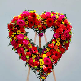 Heart-shaped floral wreath on a wooden stand with red, pink, and yellow flowers