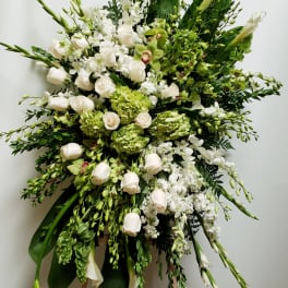 Large white and green funeral spray with roses and orchids on a stand