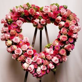Heart-shaped floral wreath of pink roses and magenta blooms on a stand