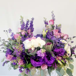Purple and pink floral arrangement with white orchids in a white vase