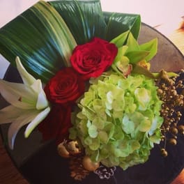 Red roses with a green hydrangea bloom and white lily on a dark plate