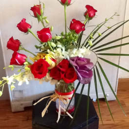 Tall bouquet of red roses and orchids in a glass vase