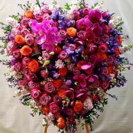 Heart-shaped floral arrangement with pink roses, orchids, and purple flowers
