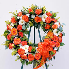 Heart-shaped wreath of orange roses and white daisies with an orange ribbon