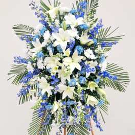 Standing floral spray with white lilies and blue flowers on an easel