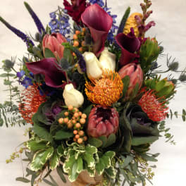 Mixed bouquet with calla lilies, protea, and purple spikes in a wrapped vase