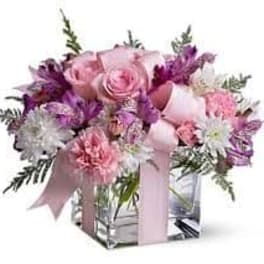 Pink and purple bouquet in a clear square vase with a ribbon