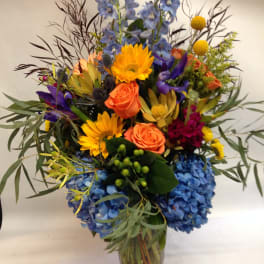 Colorful mixed bouquet in a clear glass vase with blue hydrangeas and orange roses
