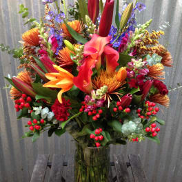 Tall mixed bouquet with lilies, calla lilies, and orange blooms in a glass vase