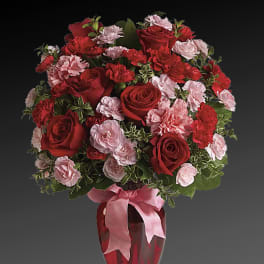 Red roses and pink carnations in a red vase with a pink ribbon