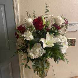 Tall bouquet of red and white roses with white lilies in a glass vase