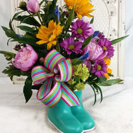 Colorful bouquet in a turquoise rain boot vase with a striped ribbon