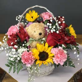 Basket arrangement with a teddy bear, sunflowers, roses, and pink carnations