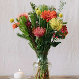 Mixed bouquet of orange and pink flowers in a clear glass vase beside a candle
