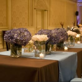 Purple hydrangea and white rose centerpieces in glass vases on a banquet table