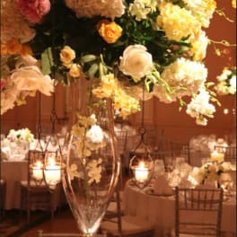 Tall floral centerpiece in a clear glass vase with hanging candle holders