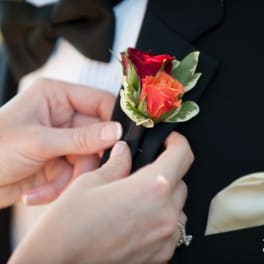 Hands pinning a rose boutonniere onto a tuxedo lapel