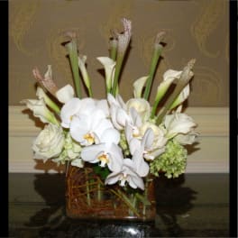 White orchids and calla lilies arranged in a square glass vase