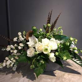 White floral arrangement with berries and feathers in a low container