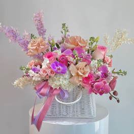 Pink and peach roses with orchids in a white wicker basket