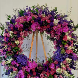 Large floral wreath with pink, purple, and white blooms on a wooden stand