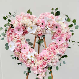 Heart-shaped floral arrangement of pink and white roses with orchids and daisies