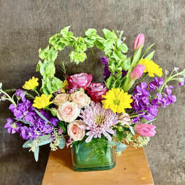 Mixed bouquet in a green glass vase with pink, yellow, and purple flowers