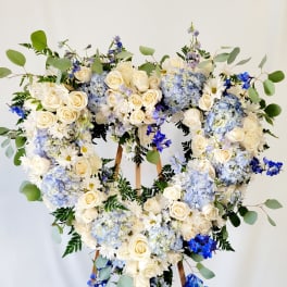 Heart-shaped floral wreath with white roses, blue hydrangeas, and daisies on an easel