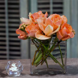Peach roses in a square glass vase beside a small candle holder