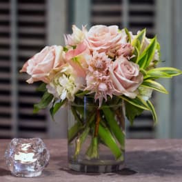 Pink roses and pale flowers arranged in a glass vase beside a small candle holder.