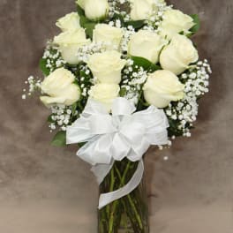 White roses arranged in a glass vase with baby's breath and a white ribbon