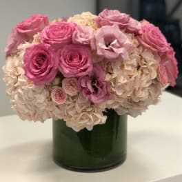 Low round arrangement of pink roses and lisianthus with blush hydrangeas in a glass cylinder vase