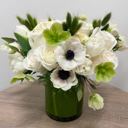 Compact arrangement of white roses and anemones with green blooms in a dark green glass vase