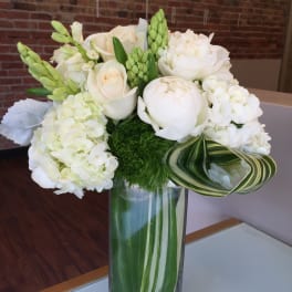 White floral arrangement in a tall glass vase with green accents