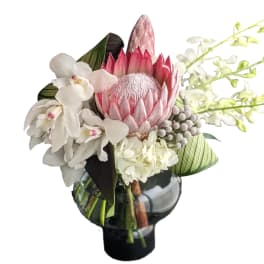 Pink protea and white orchids in a black glass vase
