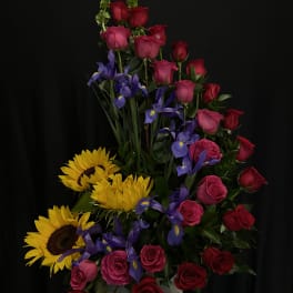 Tall arrangement of red and pink roses with purple irises and yellow sunflowers