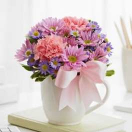 Pink and purple daisy bouquet in a white mug with a ribbon