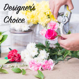Florist trimming a pink rose beside white and yellow chrysanthemums and pink carnations on a worktable.