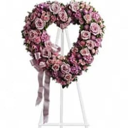 Heart-shaped pink rose wreath on a white stand with ribbon