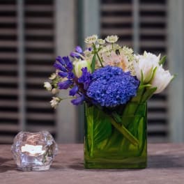 Blue and white flowers in a green glass vase beside a small candle holder