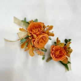 Orange rose and orchid corsage and boutonniere set with ribbon accents on a white background