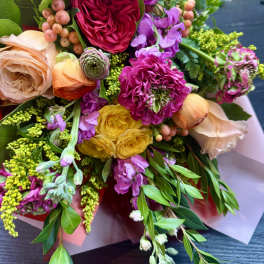 Bright hand-tied bouquet of pink, yellow, peach, and purple blooms wrapped in pastel paper