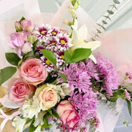 Bouquet of pink roses, purple daisies, and white lilies in pale wrapping