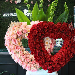 Heart-shaped rose arrangements in pink and red with tall green leaves behind them