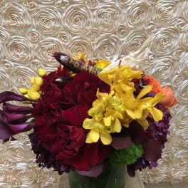 Bouquet of red roses, yellow orchids, and purple calla lilies in a glass vase