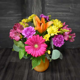 Bright mixed bouquet in an orange vase with pink, yellow, and orange flowers