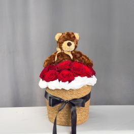Teddy bear sitting on a box of red roses with a black ribbon
