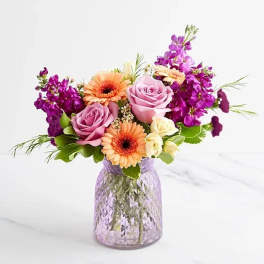 Pink roses and orange gerbera daisies in a purple glass vase