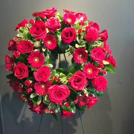 Heart-shaped wreath of red roses and pink daisies on a stand