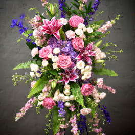 Tall floral spray with pink roses, lilies, and purple blooms on a stand